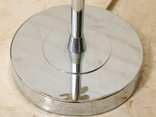 Load image into Gallery viewer, A close-up of a polished chrome lamp base with a circular metal shade and central stem, resting on a beige stone surface.
