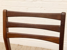 Load image into Gallery viewer, Close-up of a mid-century modern wooden chair back with a warm brown finish, set against a white brick wall background.
