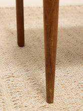 Load image into Gallery viewer, Close-up of a wooden table leg standing on a textured cream woven rug.
