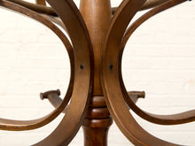 Load image into Gallery viewer, Close-up of a wooden chair or stool base with curved armrests or support arms, shown against a white painted brick wall.
