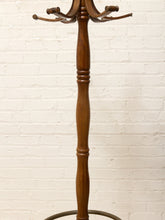 Load image into Gallery viewer, A tall wooden coat rack with multiple curved hooks and a round base, shown against a white painted brick wall.
