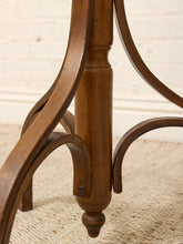 Load image into Gallery viewer, Close-up of a wooden table leg with curved arms and a turned central post, shown on a light beige carpet against a white brick wall.
