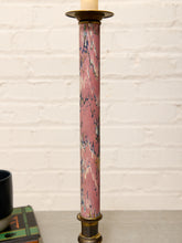 Load image into Gallery viewer, A tall candlestick holder with a pink and blue marbled patterned column and brass-toned metal base and top, shown standing on a tabletop against a white brick wall.
