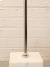 Load image into Gallery viewer, A polished chrome metal pole mounted on a square white marble base, set against a white painted brick wall background.
