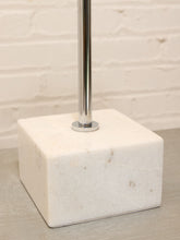 Load image into Gallery viewer, A square white marble lamp base with a polished chrome metal pole rising from the center, set against a white brick wall background.

