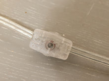 Load image into Gallery viewer, A close-up of a clear plastic connector or bead with a small metallic screw detail, threaded onto a transparent cable over a light gray textured surface.
