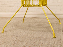 Load image into Gallery viewer, Yellow metal wire chair legs and part of the seat frame on a beige woven rug against a white brick wall.
