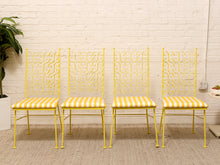 Load image into Gallery viewer, Four yellow metal dining chairs with striped yellow and white cushions, arranged side-by-side against a white brick wall.
