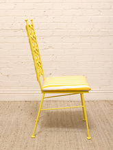 Load image into Gallery viewer, A yellow metal dining chair with a white cushion featuring yellow stripes, set against a white brick wall and a beige woven rug.
