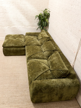 Load image into Gallery viewer, An olive green velvet sectional sofa with a matching ottoman, styled in a room with white brick walls and a beige rug.
