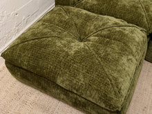 Load image into Gallery viewer, An olive green tufted floor cushion made of textured fabric, shown in a close-up view on a light-colored rug next to a white brick wall.
