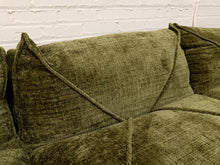 Load image into Gallery viewer, Close-up of an olive green textured fabric sofa cushion with geometric stitched paneling, set against a white brick wall background.

