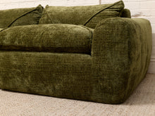 Load image into Gallery viewer, An olive green textured fabric sofa with matching cushions, positioned against a white brick wall on a beige carpet.
