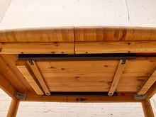 Load image into Gallery viewer, Close-up underside of a wooden table showing the natural wood grain, support beams, and metal hardware against a white brick wall background.
