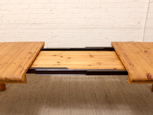 Load image into Gallery viewer, A rustic wooden folding table with a natural log edge and a light pine center panel, shown partially extended against a white brick wall and beige rug.
