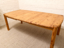 Load image into Gallery viewer, A low wooden table with a light natural wood grain tabletop and matching legs, positioned in a room with a white brick wall and textured beige carpet.

