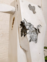 Load image into Gallery viewer, A close-up of a white painted wooden post or frame with significant peeling and chipped paint, showing the textured dark surface beneath. A white brick wall is visible in the background.

