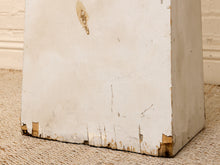 Load image into Gallery viewer, A close-up of a distressed white wooden block or pedestal base with chipped paint and visible wood showing at the edges, resting on a beige woven rug.
