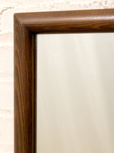 Load image into Gallery viewer, Close-up of a dark brown wooden mirror frame with a smooth, polished finish, set against a light beige brick wall.

