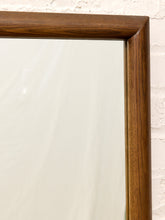 Load image into Gallery viewer, Close-up of a rectangular mirror with a thick, warm brown wooden frame, set against a white brick wall.
