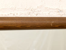 Load image into Gallery viewer, A close-up of a medium brown wood grain trim or molding bar against a textured off-white plaster wall.
