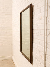 Load image into Gallery viewer, A tall, narrow rectangular wall mirror with a dark brown wooden frame, mounted on a white painted brick wall.

