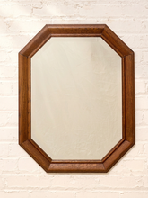 Load image into Gallery viewer, An octagonal wall mirror with a medium brown wooden frame, mounted on a white painted brick wall.
