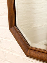 Load image into Gallery viewer, Close-up of a hexagonal wall mirror with a thick, dark brown wooden frame, mounted on a white painted brick wall.
