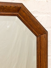 Load image into Gallery viewer, Close-up of a wooden mirror frame corner with a warm medium-brown wood grain finish, showing the edge of a mirror against a white painted brick wall.
