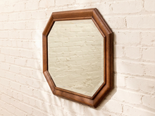 Load image into Gallery viewer, An octagonal wall mirror with a medium brown wooden frame, mounted on a white painted brick wall.
