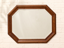 Load image into Gallery viewer, An octagonal wall mirror with a medium brown wooden frame, mounted on a white painted brick wall.
