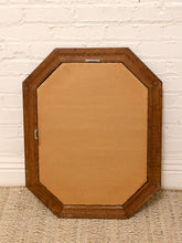 Load image into Gallery viewer, An octagonal wooden mirror frame with a natural light wood backing, leaning against a white brick wall on a woven rug.
