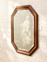 Load image into Gallery viewer, An octagonal wall mirror with a warm brown wooden frame, mounted on a white painted brick wall with soft leaf shadows.
