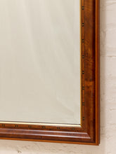 Load image into Gallery viewer, Close-up of a large wall mirror with a richly carved brown wooden frame and brass nailhead trim, mounted on a white textured brick wall.

