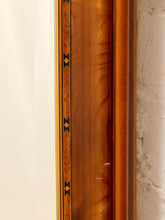 Load image into Gallery viewer, Close-up of a polished wood frame or panel with warm orange-brown grain and a narrow black-and-gold geometric inlay detail, shown against a light wall.
