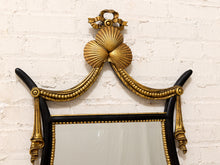 Load image into Gallery viewer, An ornate French-style wall mirror with a black frame and elaborate gilded bronze scrollwork, featuring a shell motif at the top, mounted on a white brick wall.
