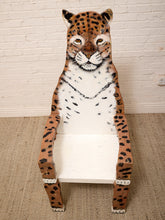 Load image into Gallery viewer, A whimsical wooden chair shaped like a leopard, featuring a painted leopard face, spots, and stripes on its body, set against a white brick wall and beige carpet.
