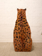 Load image into Gallery viewer, A large, whimsical leopard-shaped wooden stool or chair, viewed from the back, featuring a natural wood finish with hand-painted black leopard spots, set against a white brick wall and beige carpet.
