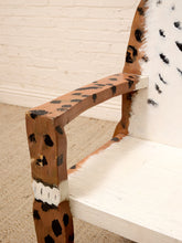 Load image into Gallery viewer, A close-up of a rustic wooden chair with a leopard print pattern on the armrests and back, combined with white painted sections, set against a white brick wall and beige carpet.
