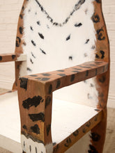 Load image into Gallery viewer, A close-up of a rustic wooden chair featuring a painted leopard print pattern with brown wood, white hide, and black spots.
