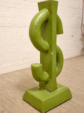 Load image into Gallery viewer, A green abstract sculpture shaped like a stylized dollar sign, standing on a matching square base against a white brick wall and beige carpet.
