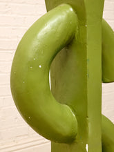Load image into Gallery viewer, A close-up of a green abstract sculpture or decorative wall art piece against a white painted brick wall.
