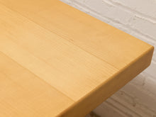 Load image into Gallery viewer, Close-up of a light natural wood tabletop corner with a white painted brick wall background.
