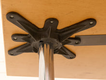 Load image into Gallery viewer, Close-up of a black metal table base with six radiating legs attached to a light wood tabletop, with a polished silver vertical support post visible.
