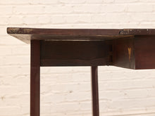 Load image into Gallery viewer, Close-up of a dark brown wooden table showing the underside of the tabletop, joinery, and legs against a white painted brick wall background.

