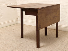 Load image into Gallery viewer, A dark brown wooden drop-leaf table with a single pull-out drawer, shown in a room setting with a white brick wall and beige carpet.
