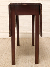 Load image into Gallery viewer, A dark brown wooden drop-leaf table with a rectangular top and four legs, shown standing on a textured beige rug against a white brick wall background.
