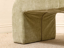 Load image into Gallery viewer, A close-up of a textured fabric upholstered furniture piece, showing a light olive green woven material with a visible seam and corner detail, set against a neutral cream wall and beige carpet.
