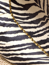 Load image into Gallery viewer, Close-up of a zebra-print fabric cushion with black and cream stripes and a diagonal line of metallic gold nailhead trim.
