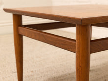 Load image into Gallery viewer, Close-up of a mid-century modern wooden table with a warm medium-brown finish, featuring a thick rectangular top, tapered legs, and a horizontal support rail.
